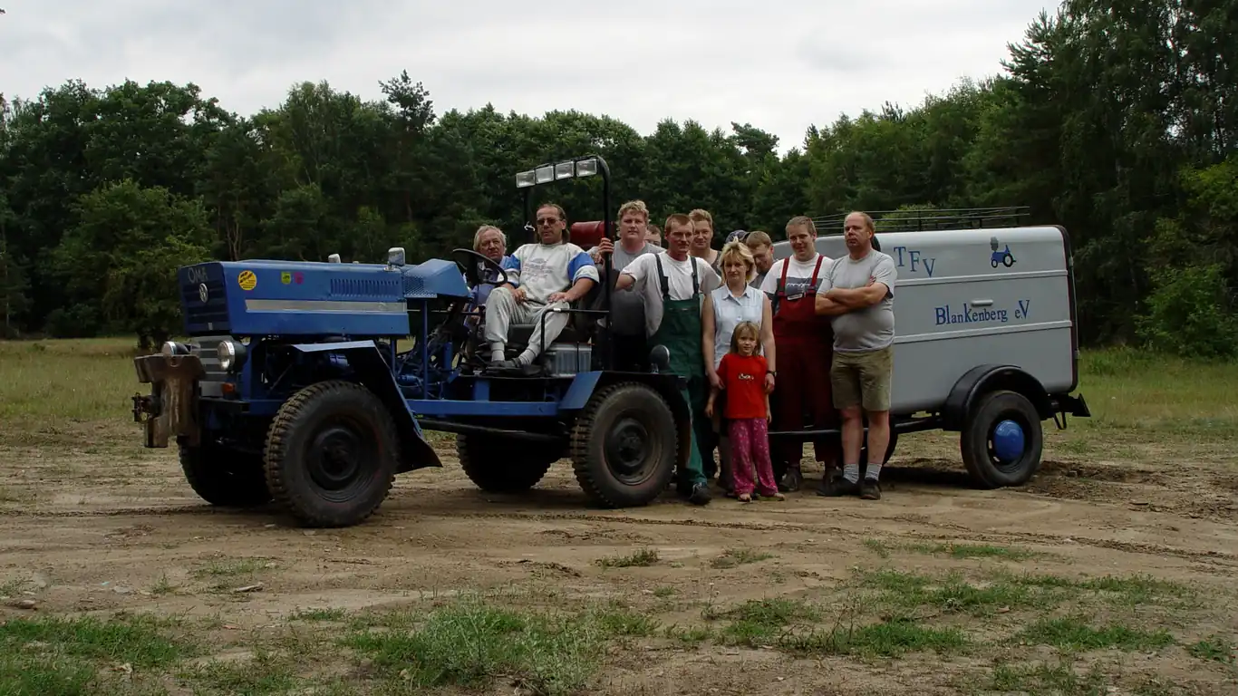 Familie posiert auf einem blauen Traktor mit Anhänger auf einer Wiese