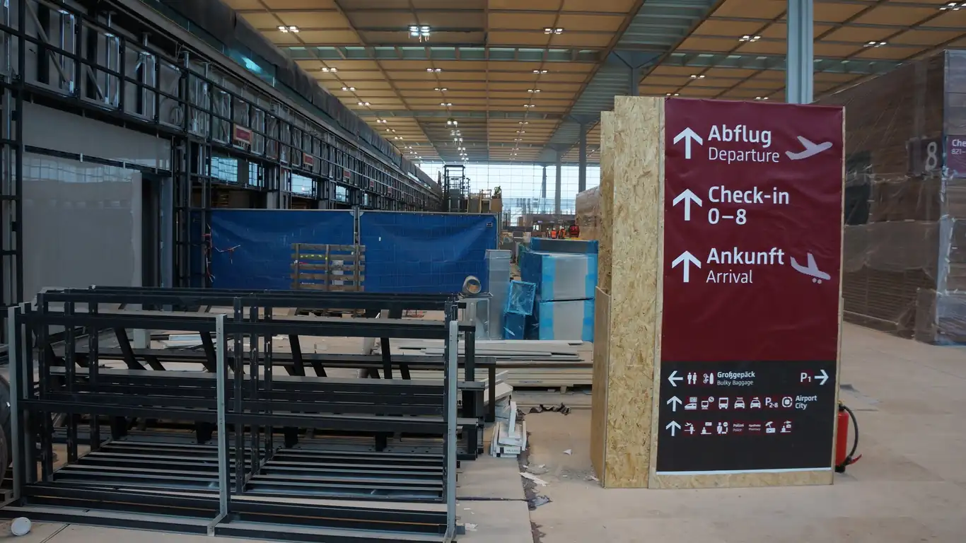 Unfertiger Check-in-Bereich im BER mit Wegweiser zu Abflug und Ankunft