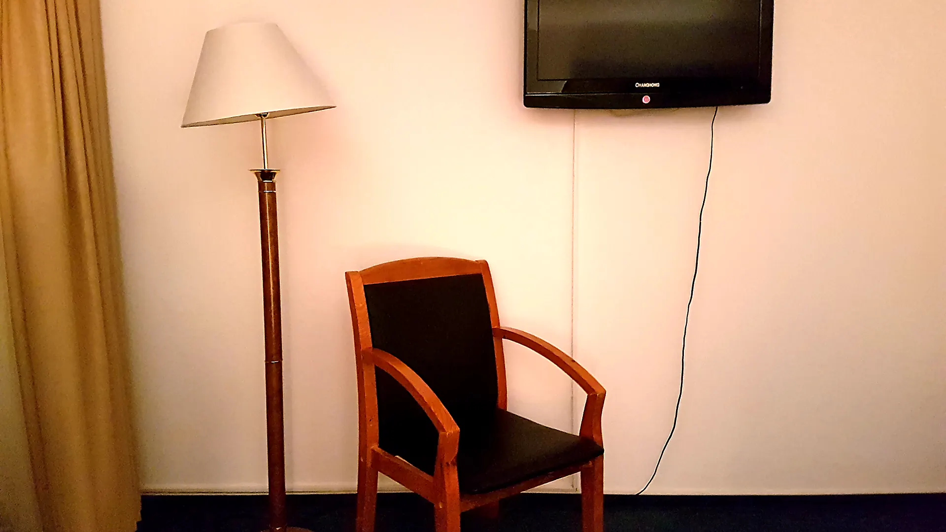 Leerer Holzstuhl vor einer Wand mit Fernseher